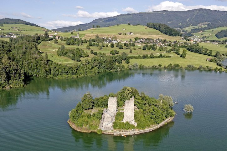 En haut, l’île d’Ogoz actuelle. En bas, une vue aérienne du site avant la mise en eau du lac (à gauche) et une reconstitution du bourg (à droite). © Charly Rappo/W. Trillen/Service archéologique de l’Etat de Fribourg