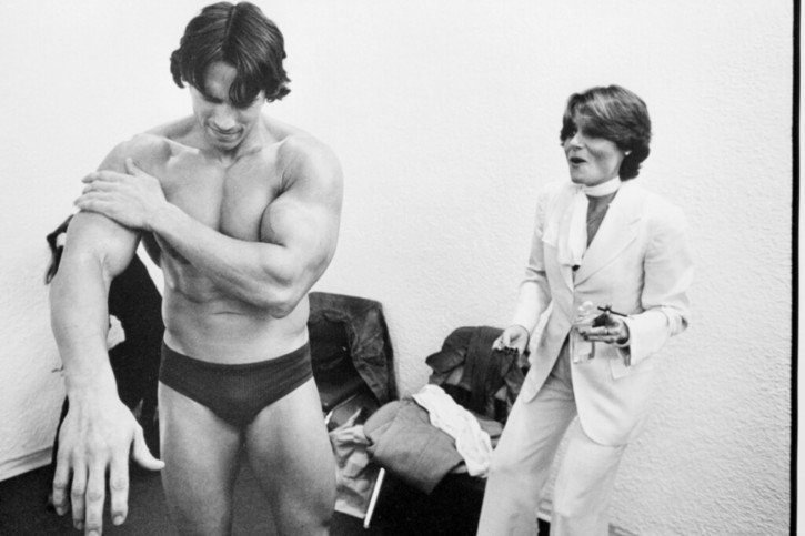 Arnold Schwarzenegger se frotte les bras avec de l'huile pour bébé en se préparant à une apparition publique lors d'une exposition sur le culturisme en tant qu'art, au Whitney Museum de New York en 1976. © KEYSTONE/AP GEORGE EASTMAN HOUSE/CANDICE BERGEN